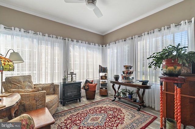 sitting room featuring hardwood / wood-style floors, crown molding, ceiling fan, and a wood stove