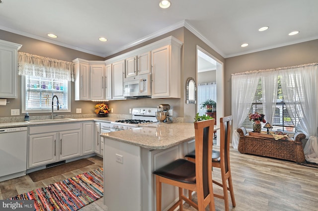 kitchen featuring a kitchen bar, sink, white cabinets, and white appliances