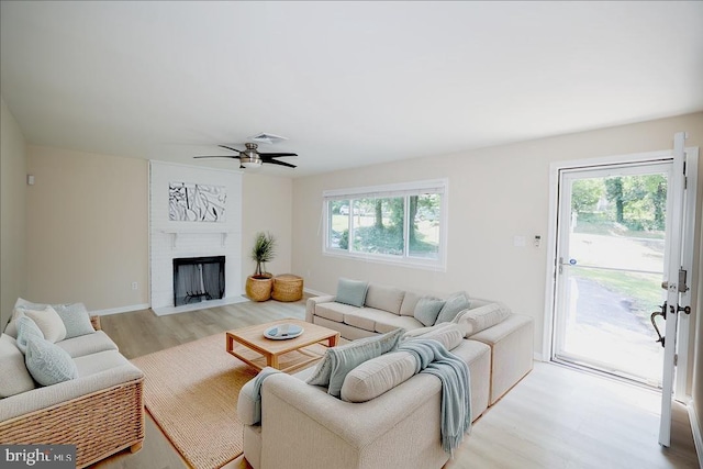 living room featuring ceiling fan, a fireplace, and light hardwood / wood-style flooring