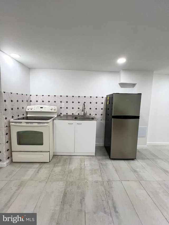 kitchen with stainless steel fridge, white electric range oven, backsplash, white cabinets, and sink