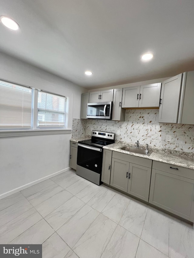 kitchen featuring sink, backsplash, appliances with stainless steel finishes, and gray cabinetry