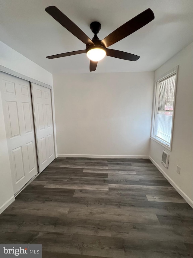 unfurnished bedroom featuring ceiling fan, a wall mounted AC, a closet, and dark hardwood / wood-style floors