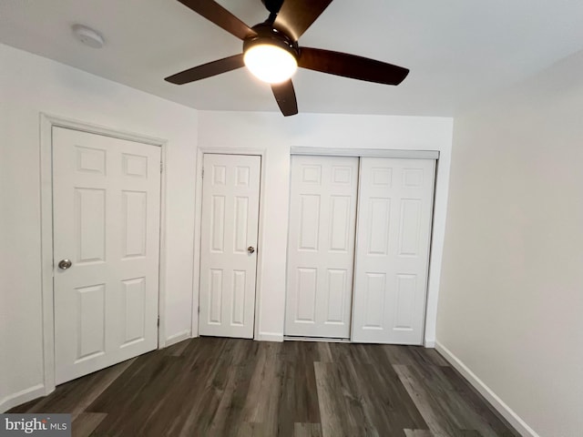 unfurnished bedroom with ceiling fan, dark hardwood / wood-style flooring, and multiple closets