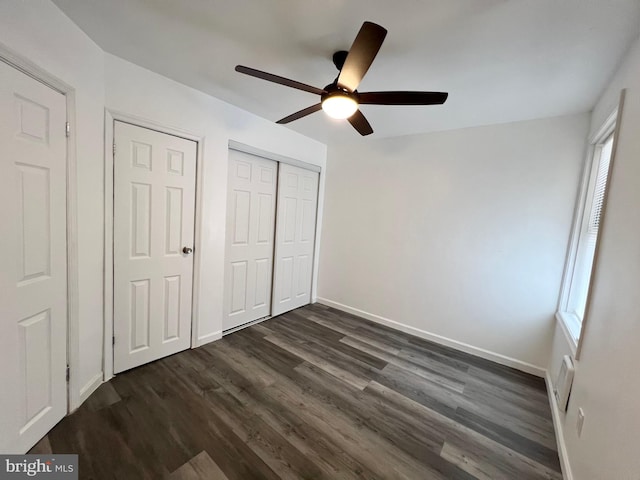 unfurnished bedroom featuring ceiling fan, dark wood-type flooring, and two closets