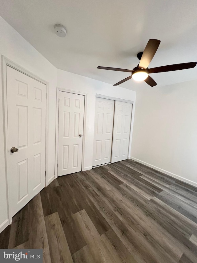 unfurnished bedroom with ceiling fan, multiple closets, and dark hardwood / wood-style flooring