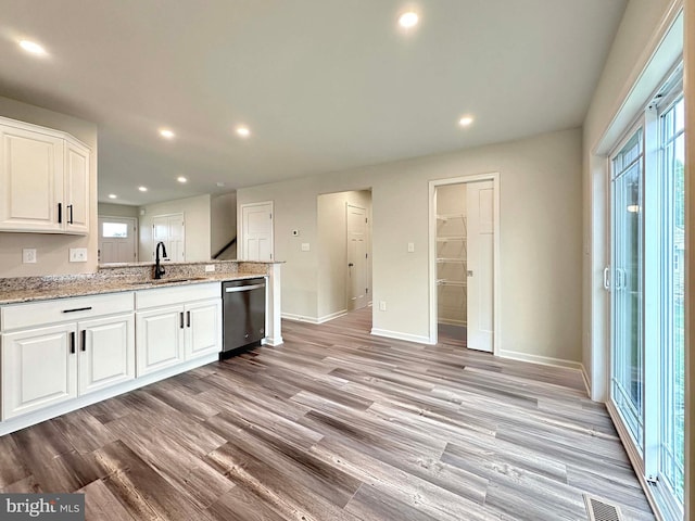 kitchen with dishwasher, sink, white cabinetry, light hardwood / wood-style flooring, and light stone counters