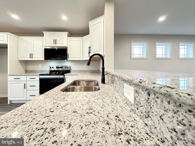 kitchen with electric stove, sink, light stone counters, and white cabinetry