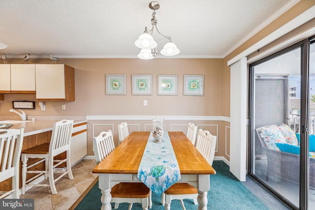 dining room with sink, a textured ceiling, ornamental molding, and an inviting chandelier