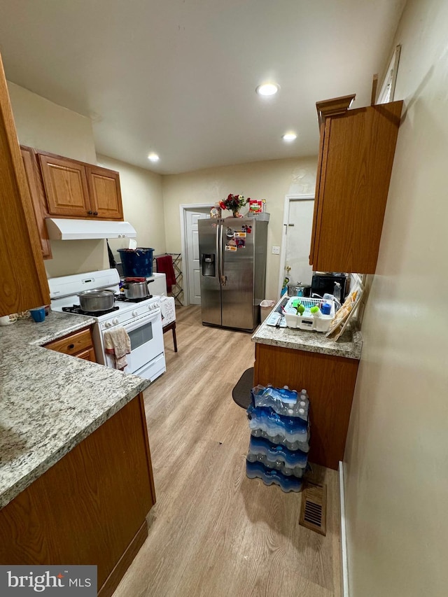 kitchen featuring stainless steel fridge with ice dispenser, light stone countertops, light wood-type flooring, and white range