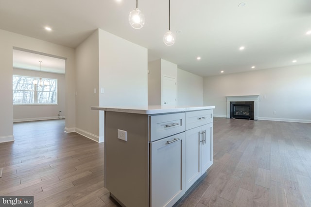 kitchen with pendant lighting, a kitchen island, an inviting chandelier, light wood-type flooring, and white cabinets