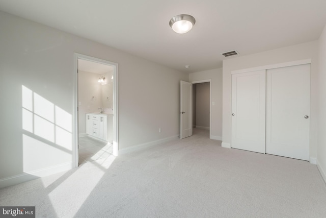 unfurnished bedroom featuring ensuite bathroom, a closet, and light carpet