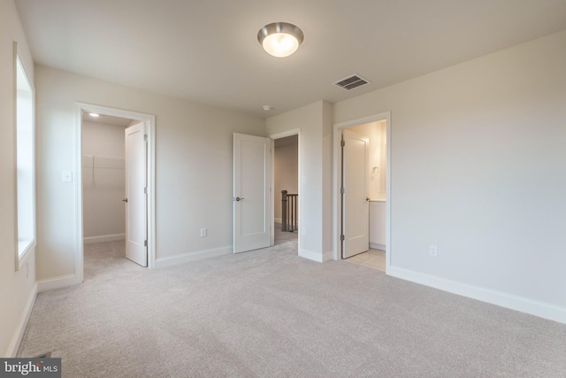 unfurnished bedroom featuring a spacious closet, a closet, connected bathroom, and light colored carpet