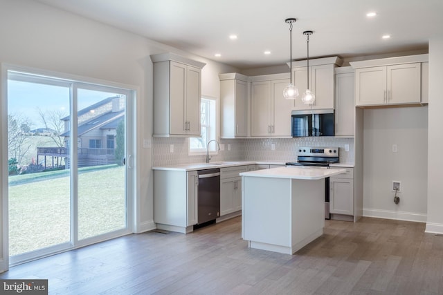 kitchen with stainless steel appliances, a kitchen island, pendant lighting, light hardwood / wood-style flooring, and sink