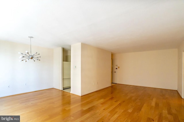 empty room with light hardwood / wood-style flooring and an inviting chandelier