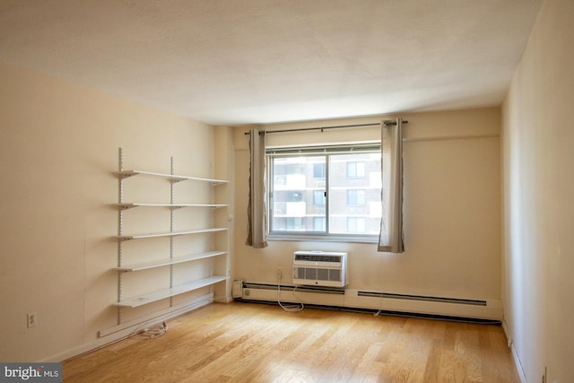 spare room with a baseboard radiator, light hardwood / wood-style floors, and an AC wall unit