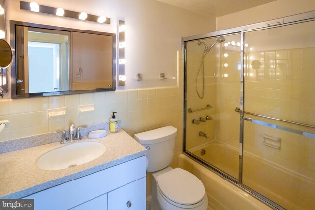 full bathroom with toilet, vanity, enclosed tub / shower combo, and tile walls