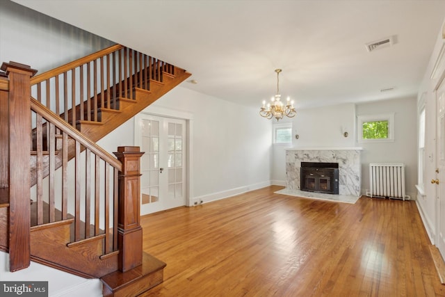 unfurnished living room with light hardwood / wood-style flooring, radiator heating unit, a premium fireplace, an inviting chandelier, and french doors