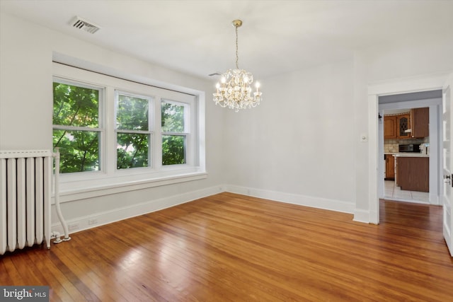 tiled spare room featuring radiator and a notable chandelier