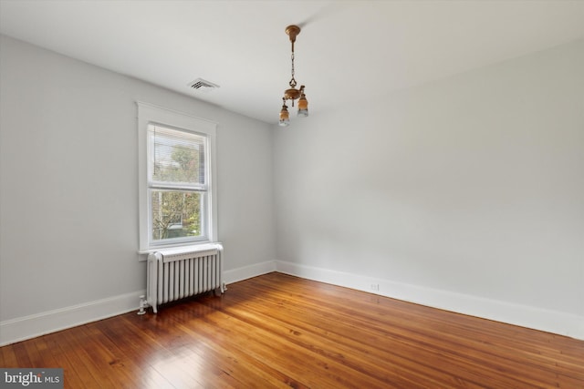 empty room with wood-type flooring, an inviting chandelier, and radiator