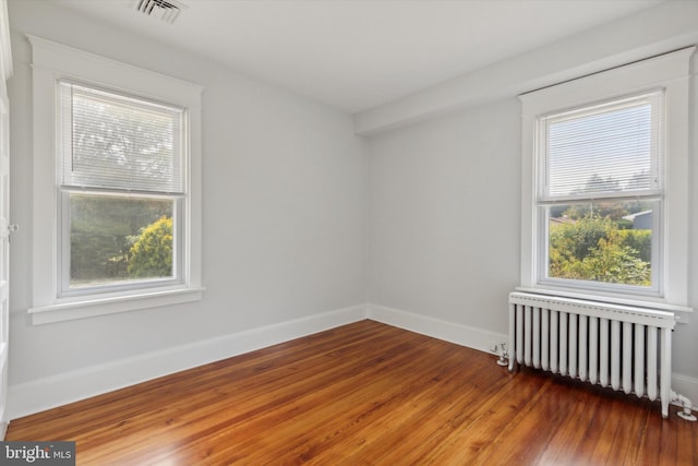 empty room with radiator, plenty of natural light, and dark wood-type flooring