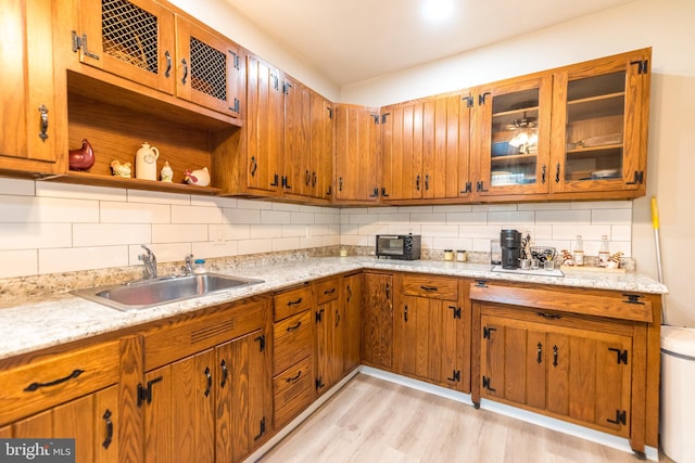 kitchen featuring a sink, backsplash, brown cabinets, open shelves, and glass insert cabinets