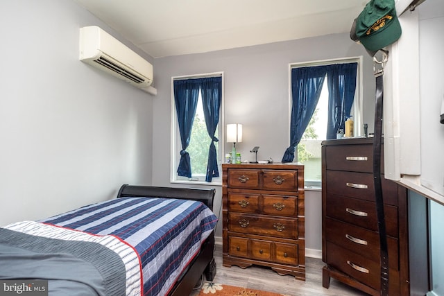 bedroom featuring a wall mounted air conditioner, light hardwood / wood-style flooring, and multiple windows