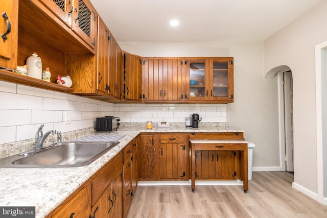 kitchen featuring light wood-type flooring, arched walkways, backsplash, and a sink