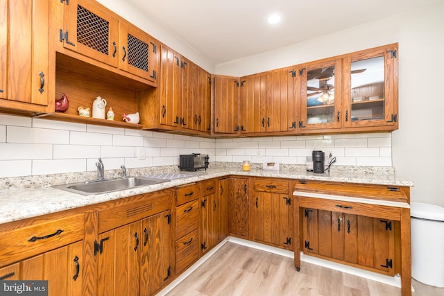 kitchen with a sink, light wood-type flooring, open shelves, tasteful backsplash, and glass insert cabinets