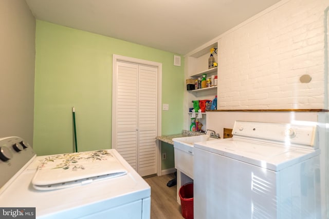 clothes washing area with laundry area, washing machine and dryer, brick wall, and wood finished floors