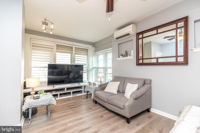 living room with a wall unit AC, light hardwood / wood-style flooring, and ceiling fan