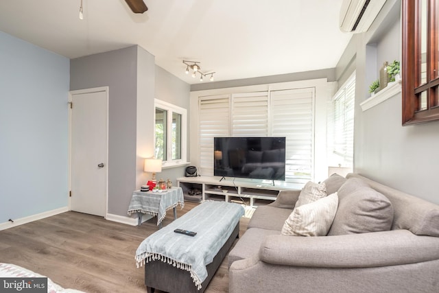 living area featuring an AC wall unit, ceiling fan, track lighting, wood finished floors, and baseboards