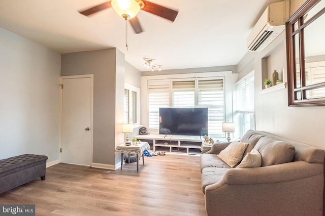 living area featuring a ceiling fan, an AC wall unit, baseboards, and light wood finished floors