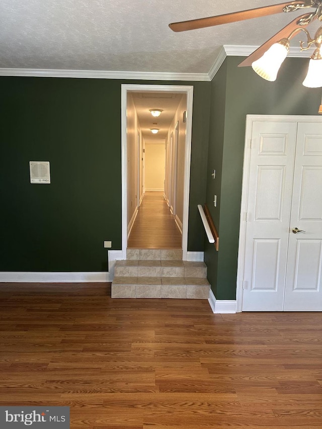 staircase featuring wood-type flooring, a textured ceiling, ornamental molding, and ceiling fan