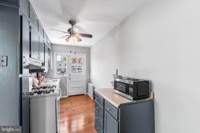 kitchen with light hardwood / wood-style floors, radiator heating unit, sink, ceiling fan, and white gas stove