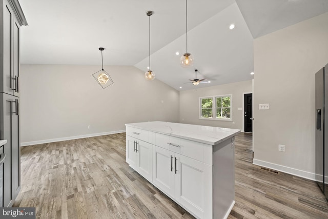 kitchen with pendant lighting, light stone counters, light hardwood / wood-style floors, white cabinets, and vaulted ceiling