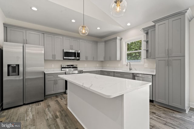 kitchen with light stone countertops, gray cabinets, stainless steel appliances, and a center island