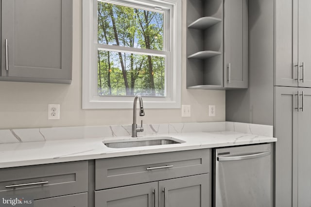 kitchen with gray cabinetry, sink, stainless steel dishwasher, and light stone countertops