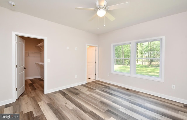 unfurnished bedroom with ceiling fan, a spacious closet, a closet, and light wood-type flooring