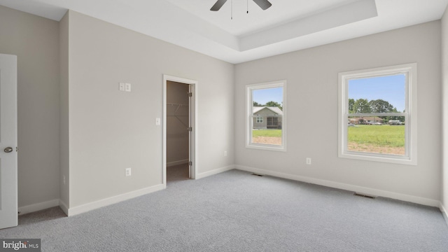 empty room featuring light carpet, a tray ceiling, and ceiling fan