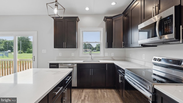 kitchen featuring sink, appliances with stainless steel finishes, hanging light fixtures, dark brown cabinetry, and light hardwood / wood-style floors