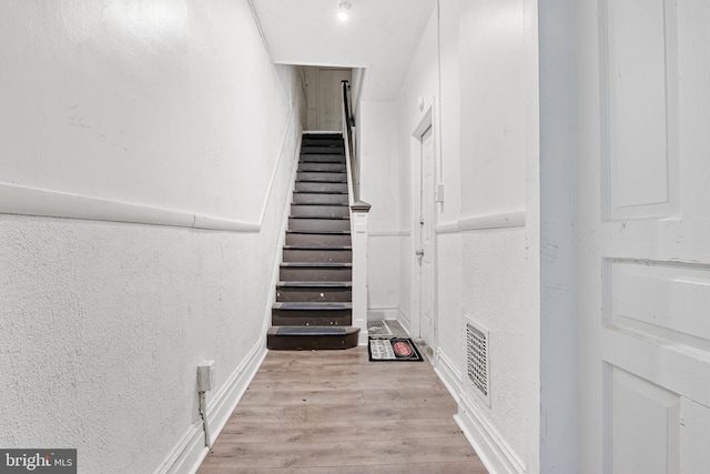 staircase featuring visible vents, wood finished floors, and a textured wall