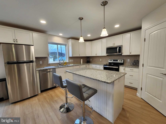 kitchen featuring sink, appliances with stainless steel finishes, white cabinets, a kitchen island, and decorative light fixtures