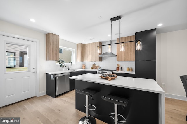 kitchen featuring decorative light fixtures, dishwasher, wall chimney range hood, a kitchen island, and a breakfast bar area