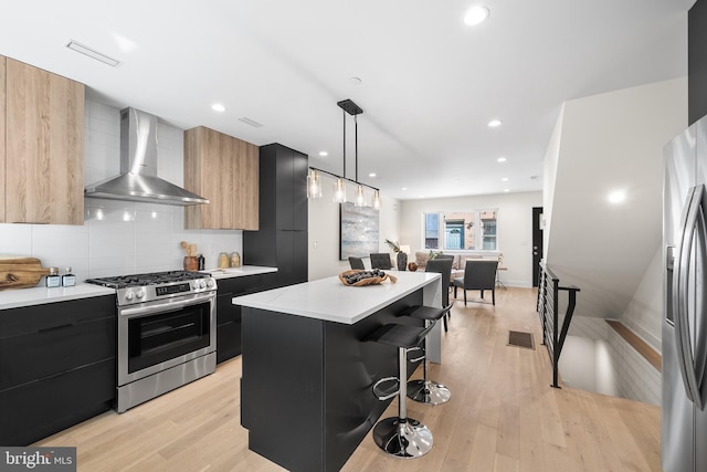 kitchen with appliances with stainless steel finishes, a kitchen breakfast bar, hanging light fixtures, wall chimney exhaust hood, and a center island