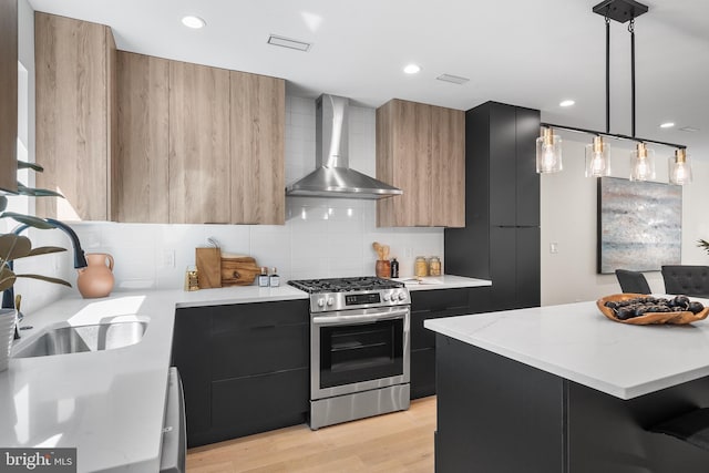 kitchen featuring decorative light fixtures, wall chimney range hood, sink, light wood-type flooring, and stainless steel range with gas stovetop