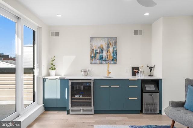 bar with sink, light wood-type flooring, blue cabinetry, and wine cooler