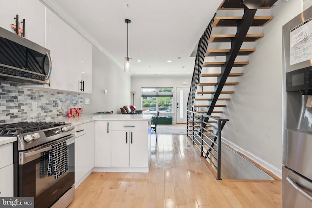 kitchen with decorative light fixtures, kitchen peninsula, decorative backsplash, stainless steel appliances, and white cabinets