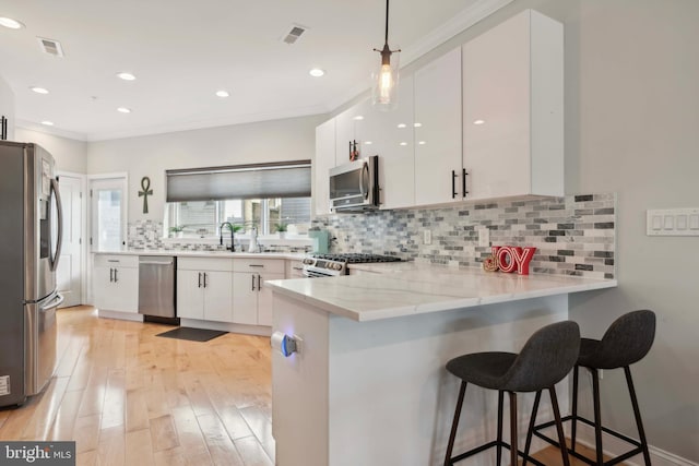 kitchen with a breakfast bar, kitchen peninsula, hanging light fixtures, stainless steel appliances, and white cabinets