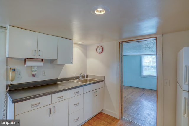 kitchen with white cabinetry, fridge, light parquet flooring, and sink