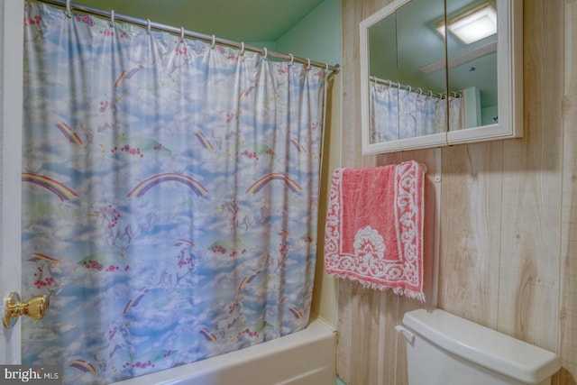 bathroom featuring wooden walls, shower / tub combo with curtain, and toilet